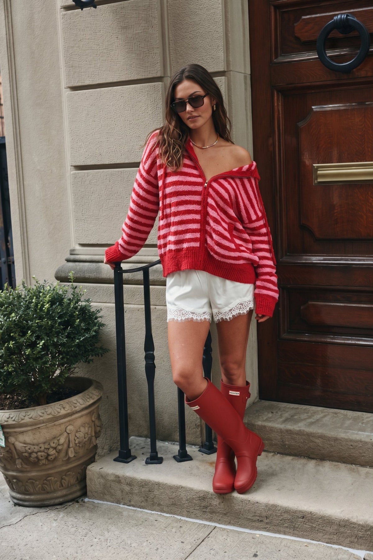 Women’s red and pink striped fuzzy knit zip-up hoodie featuring a soft textured finish, relaxed oversized fit, attached hood with drawstrings, front zipper closure, long sleeves, front pockets, and contrasting red ribbed cuffs and hem.