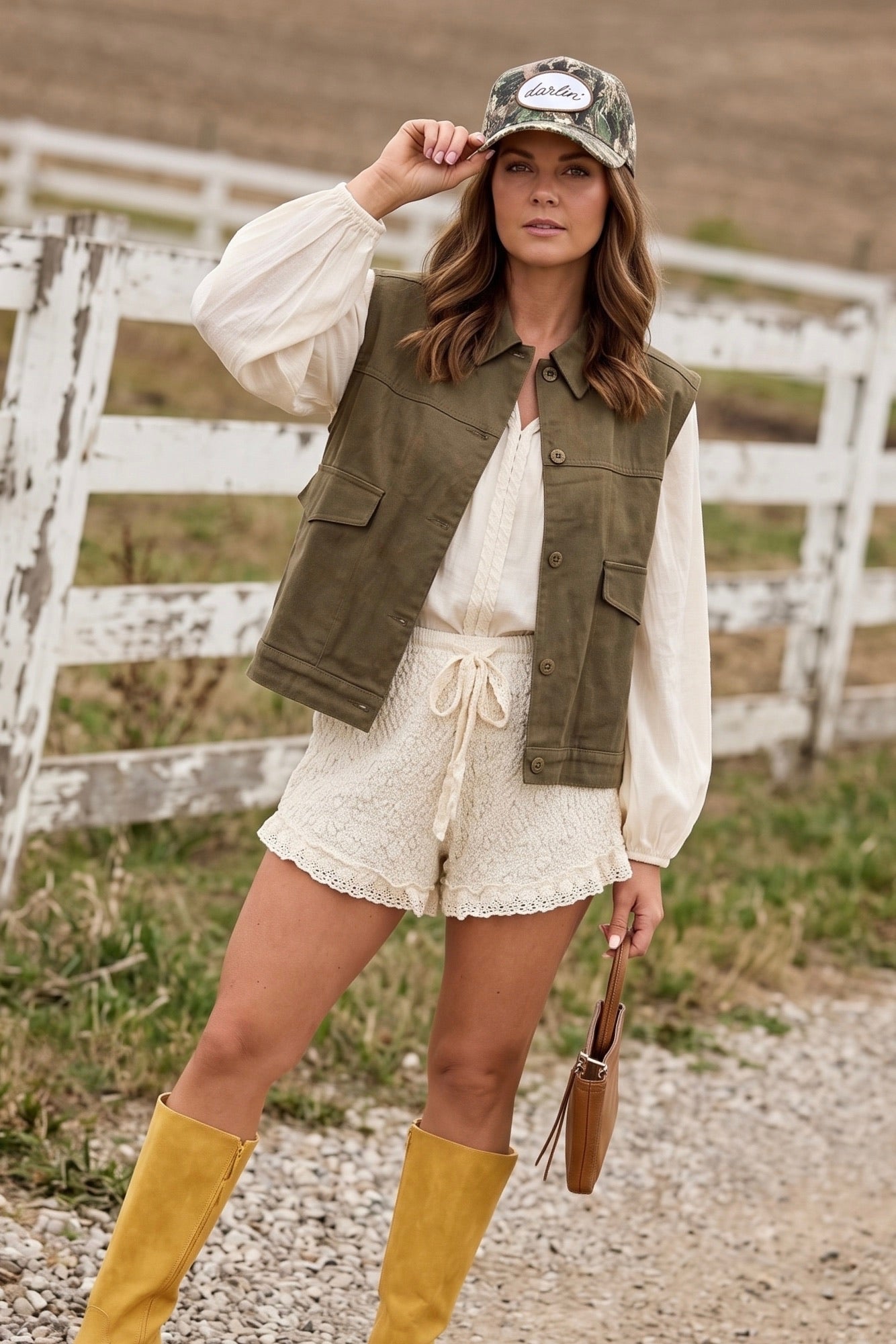 Cream textured knit shorts with elastic drawstring waistband and delicate lace trim hem, styled with a flowy blouse, olive utility vest, and western-inspired boots.