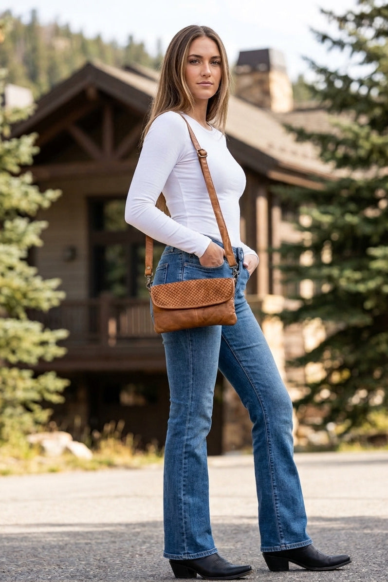 Tan genuine leather woven crossbody bag with adjustable shoulder strap styled with jeans and a white long sleeve top.