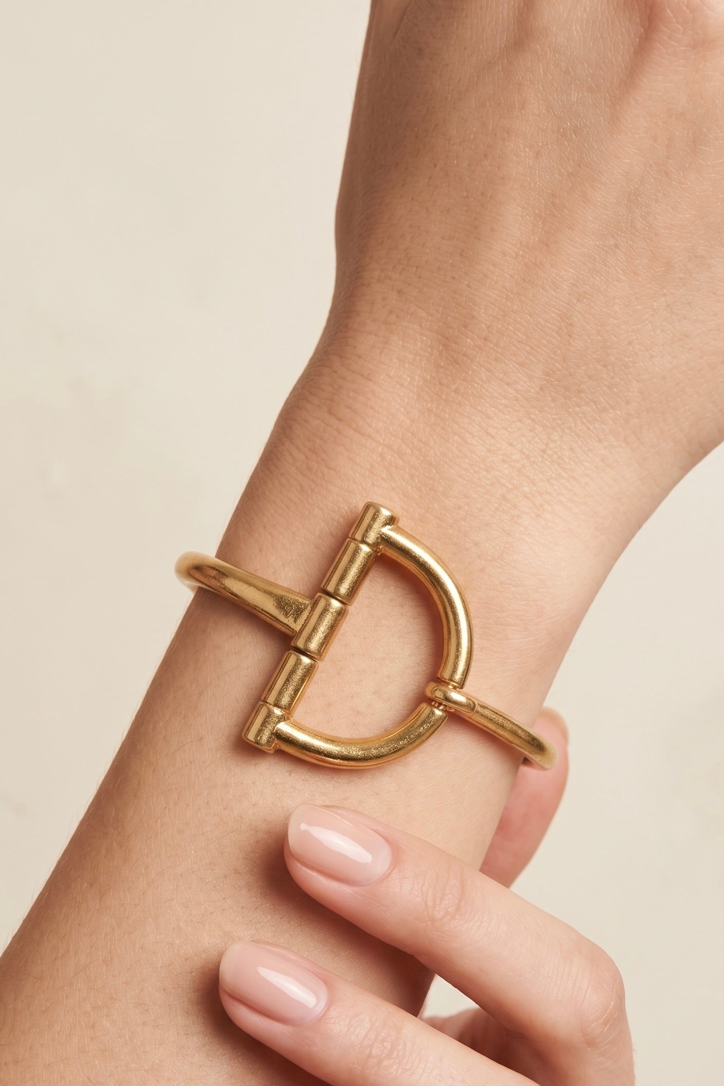 Worn gold tone horsebit cuff bracelet with sculptural equestrian-inspired front detail and open hook design.