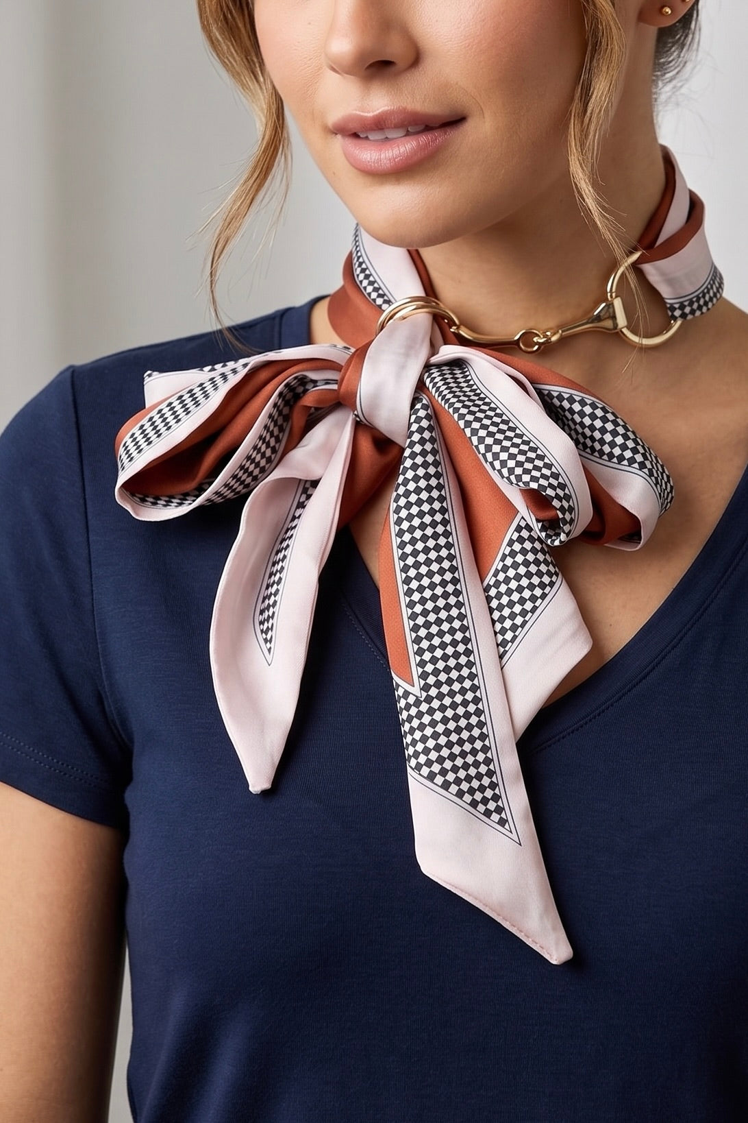 Silky red and blush pink checker print scarf necklace featuring polished gold horsebit hardware styled as a chic equestrian-inspired neck accessory.