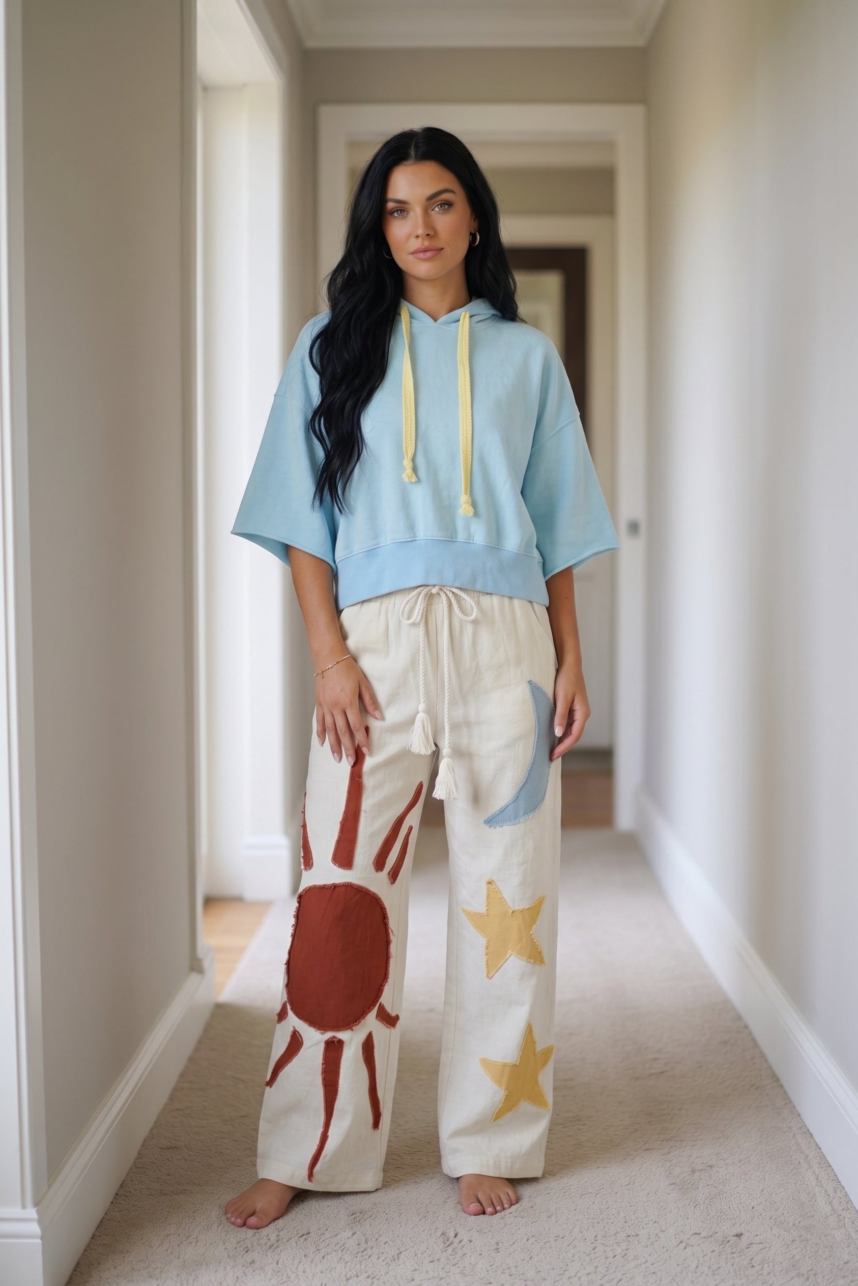 Cream wide leg pants with drawstring waist and colorful sun, moon, and star patchwork appliqué details.