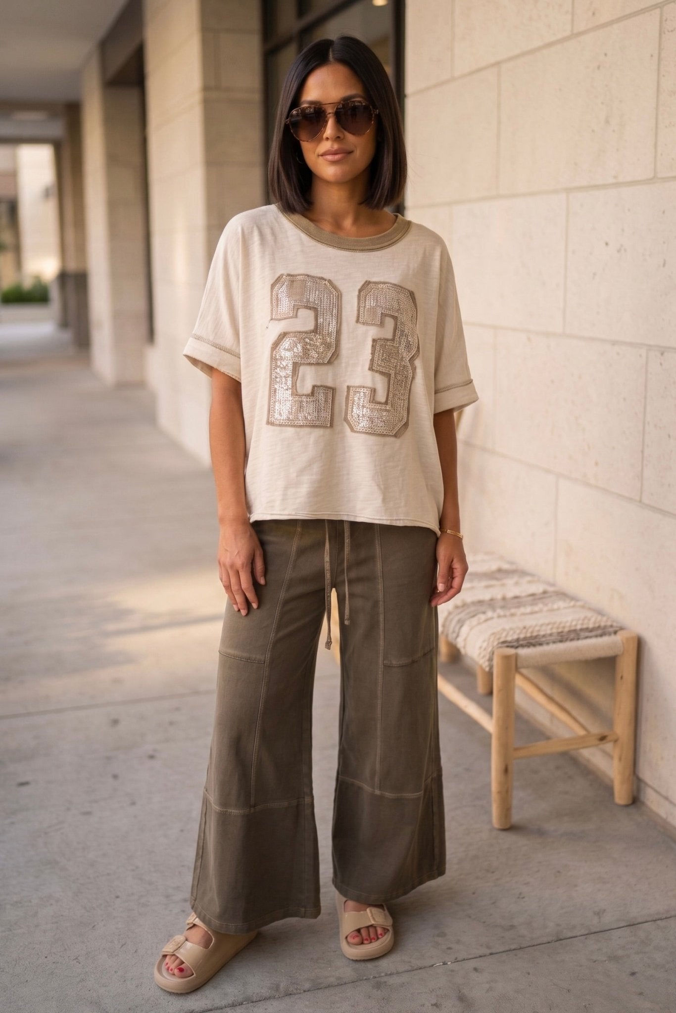 Neutral oversized boho boutique tee with sequin 23 graphic paired with olive wide leg lounge pants and slip-on sandals for a casual everyday street style look.