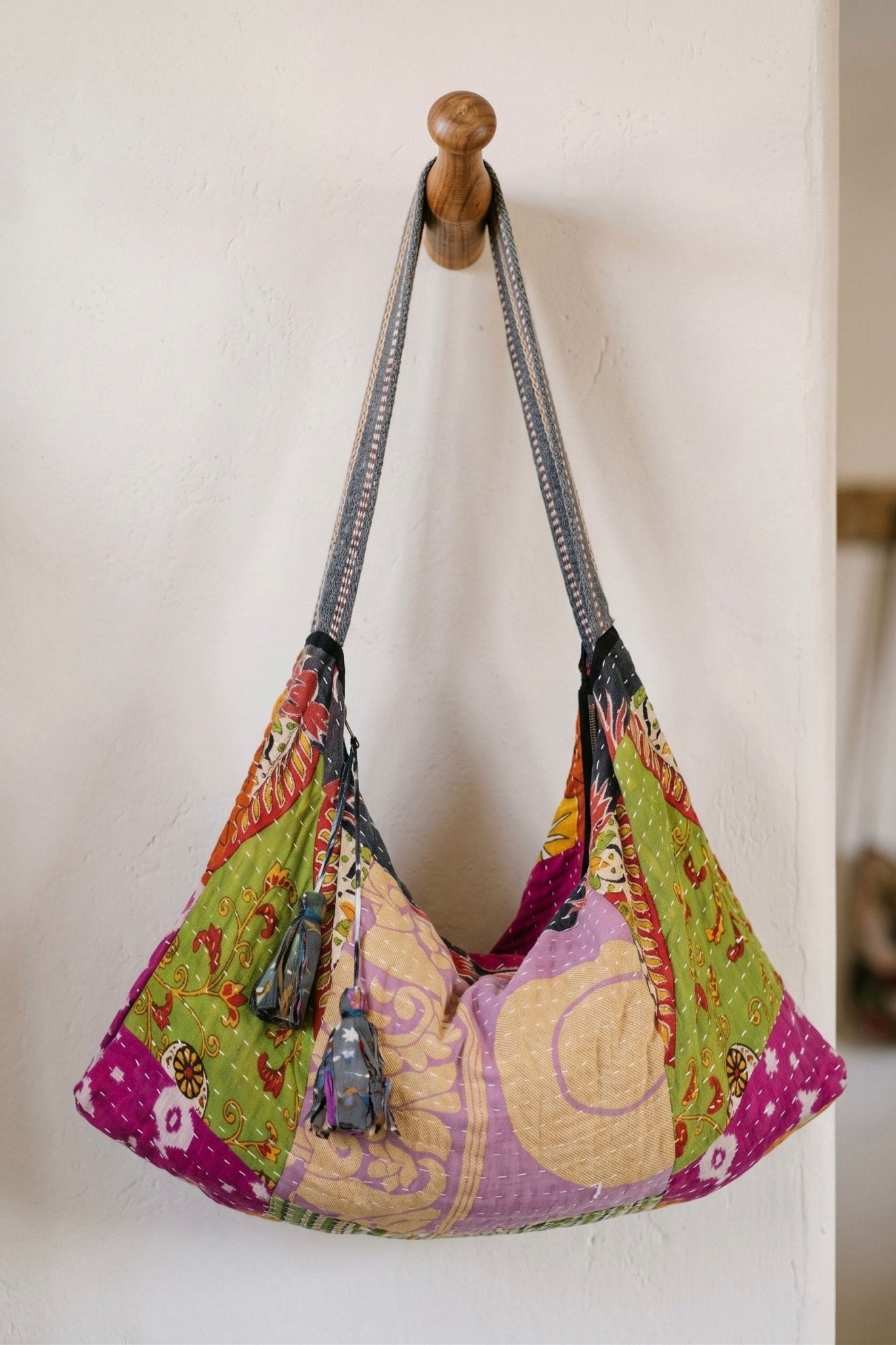 Handmade Kantha hobo bag crafted from upcycled cotton sari fabric featuring colorful patchwork patterns, hand stitching, tassel details, and a slouchy bohemian silhouette.