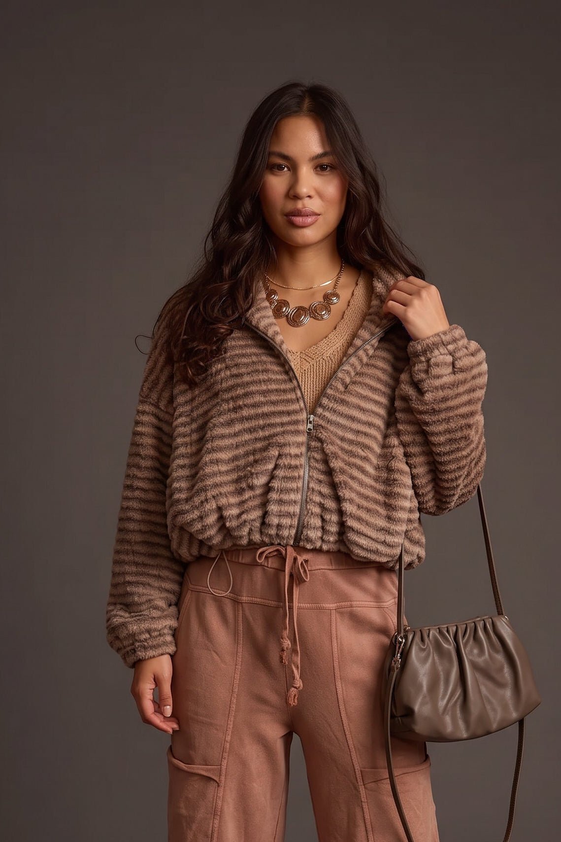 Woman wearing a taupe brown striped plush faux fur cropped jacket featuring a front zipper, oversized collar, and relaxed long sleeves, styled with wide-leg pants.