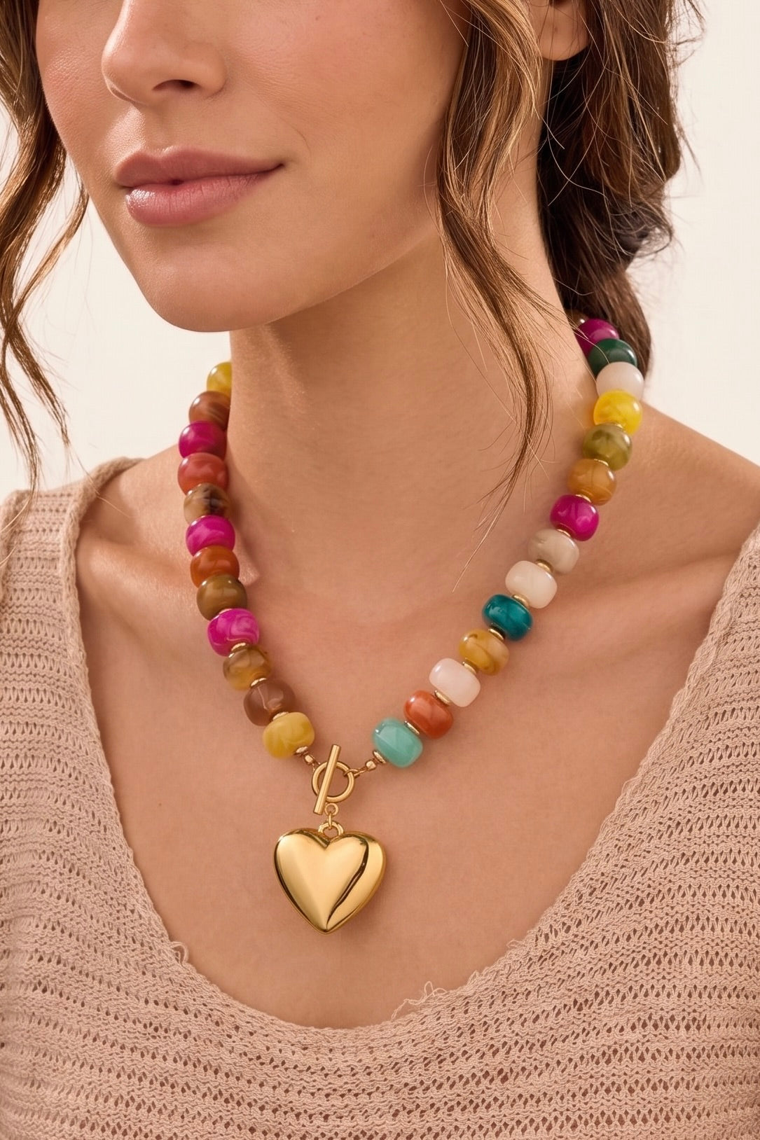 Gold-plated necklace featuring colorful mixed beads, a bold heart charm pendant, and a front toggle clasp. Each necklace features a unique combination of bead colors.