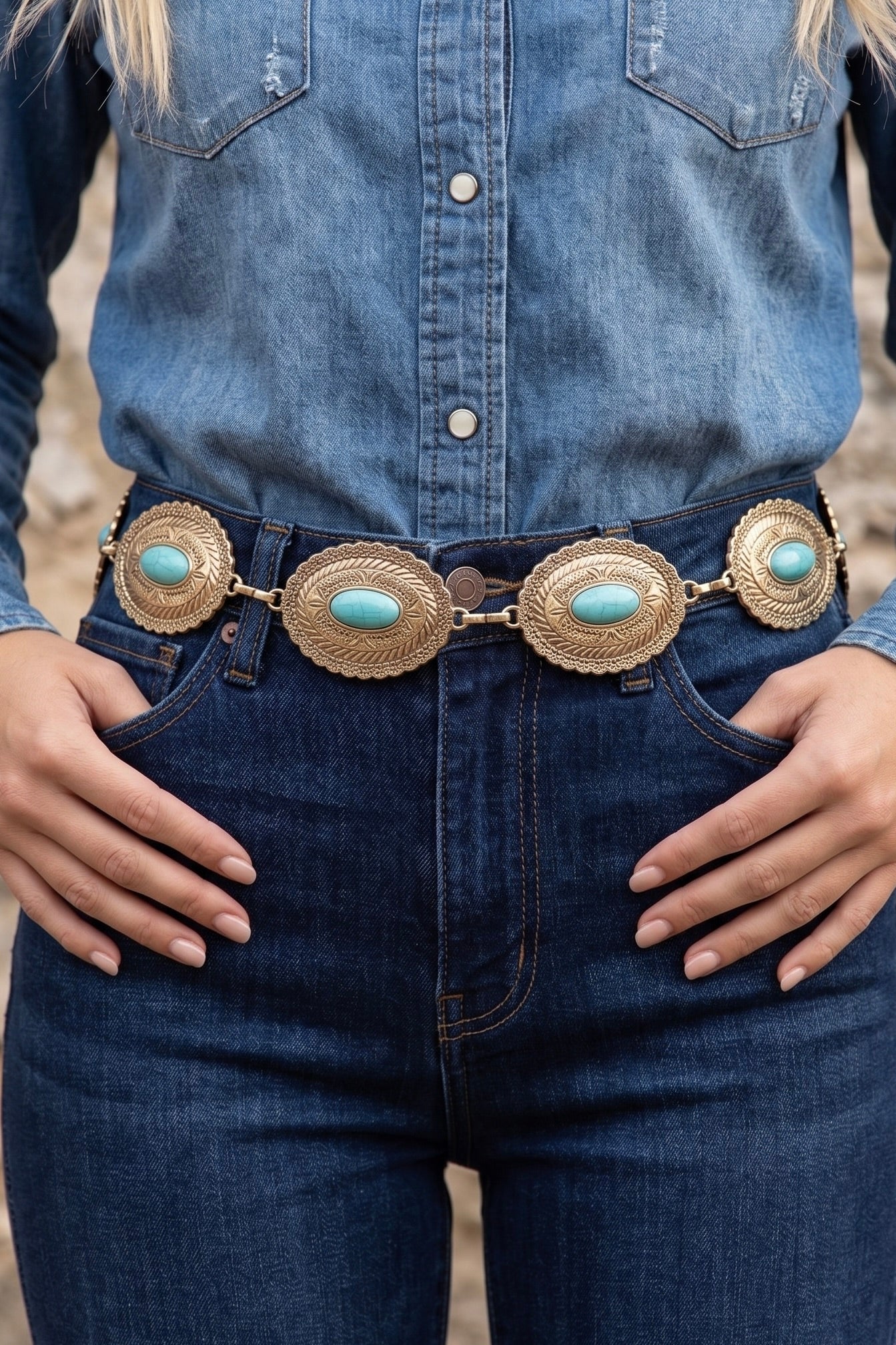 Western gold-tone chain concho belt with engraved oval conchos and turquoise center stones worn around the waist over a jeans.