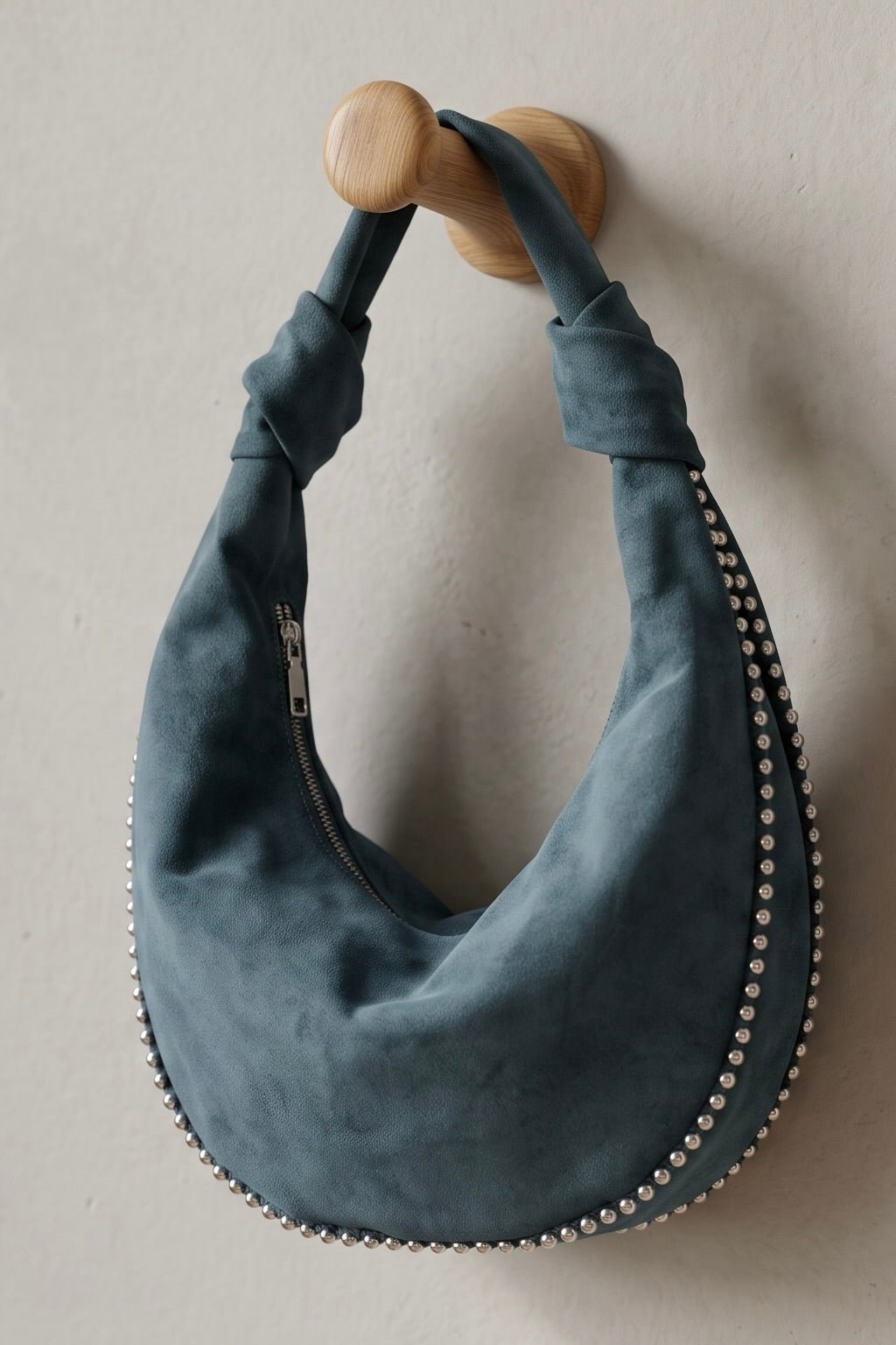Blue vegan suede crescent hobo bag with silver metal ball trim, knotted shoulder strap, and zip-top closure.