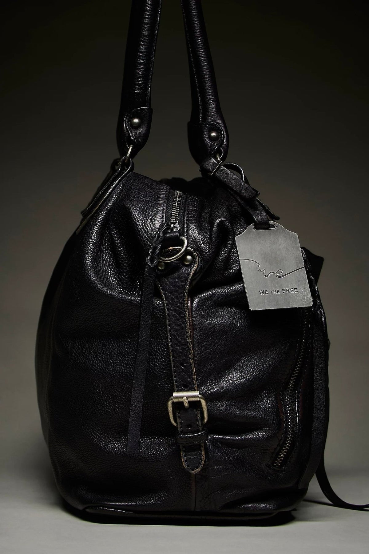 We The Free by Free People Emerson Tote Bag, a slouchy washed leather women’s carryall featuring a spacious interior, exterior zipper compartments, multiple pockets, buckle details, two top handles, adjustable detachable shoulder strap and zipper closure, available in Black, Saddle and Rusty Red.