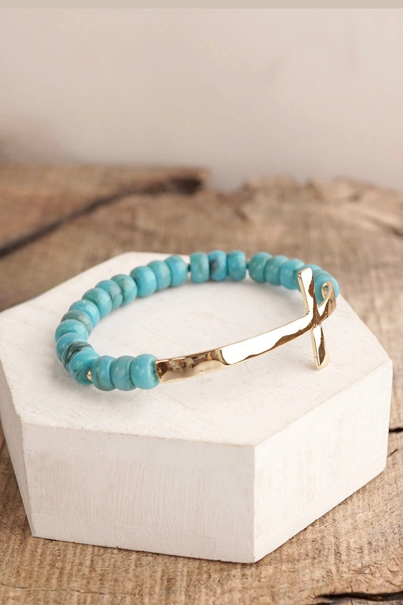 Turquoise-look rondelle bead stretch bracelet with a large hammered gold-tone cross accent.