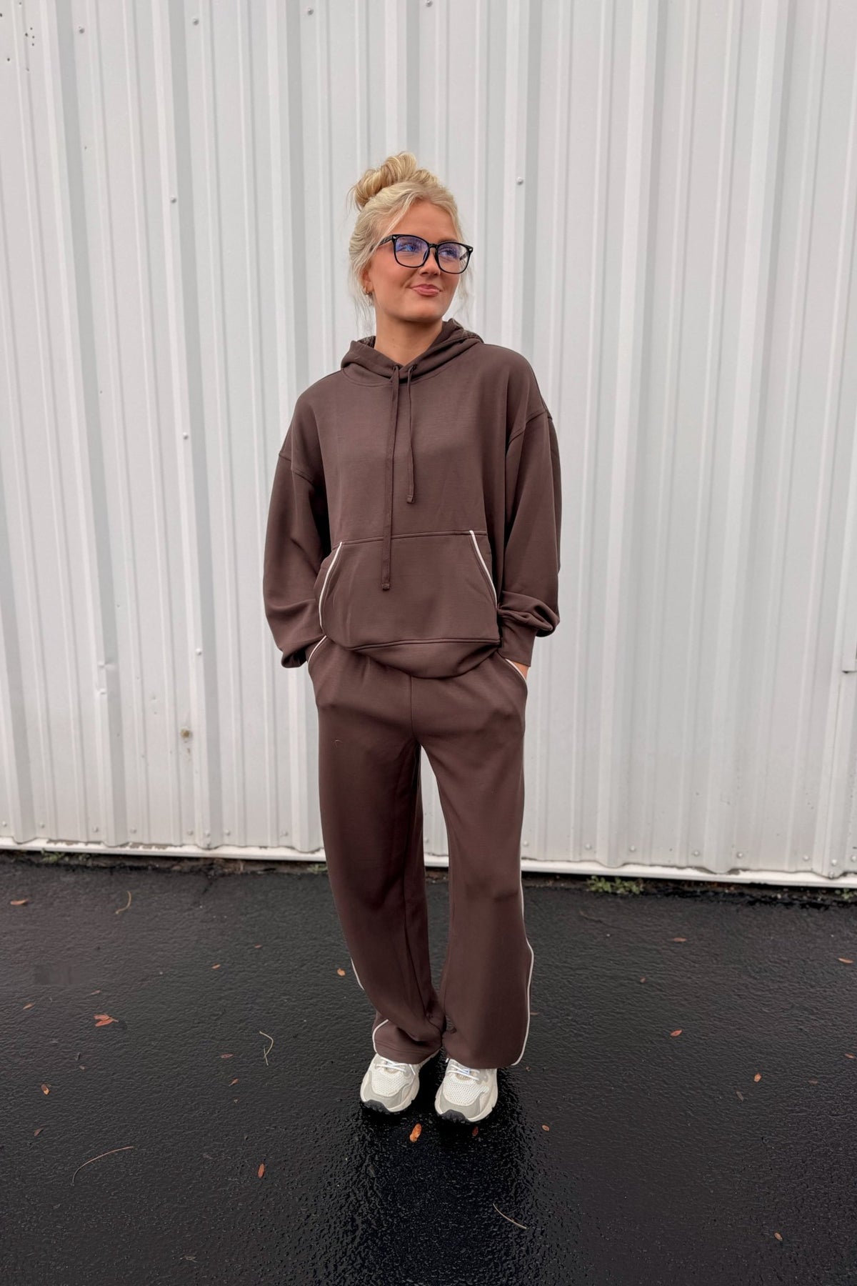 Women’s chocolate brown pullover hoodie featuring a relaxed oversized fit, drawstring hood, dropped shoulders, long sleeves, front kangaroo pocket, and contrast ivory piping detail along the pocket and sides. Coordinating chocolate brown wide-leg sweatpants are available separately for a matching lounge set.