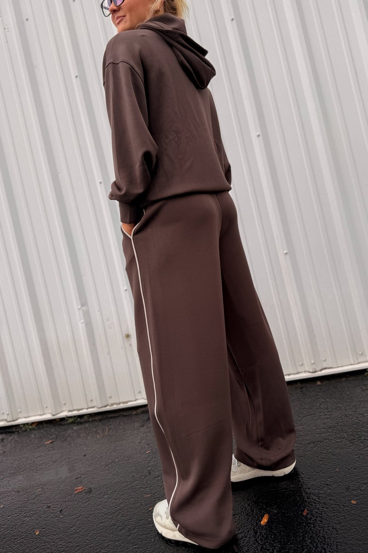 Women’s chocolate brown pullover hoodie featuring a relaxed oversized fit, drawstring hood, dropped shoulders, long sleeves, front kangaroo pocket, and contrast ivory piping detail along the pocket and sides. Coordinating chocolate brown wide-leg sweatpants are available separately for a matching lounge set.