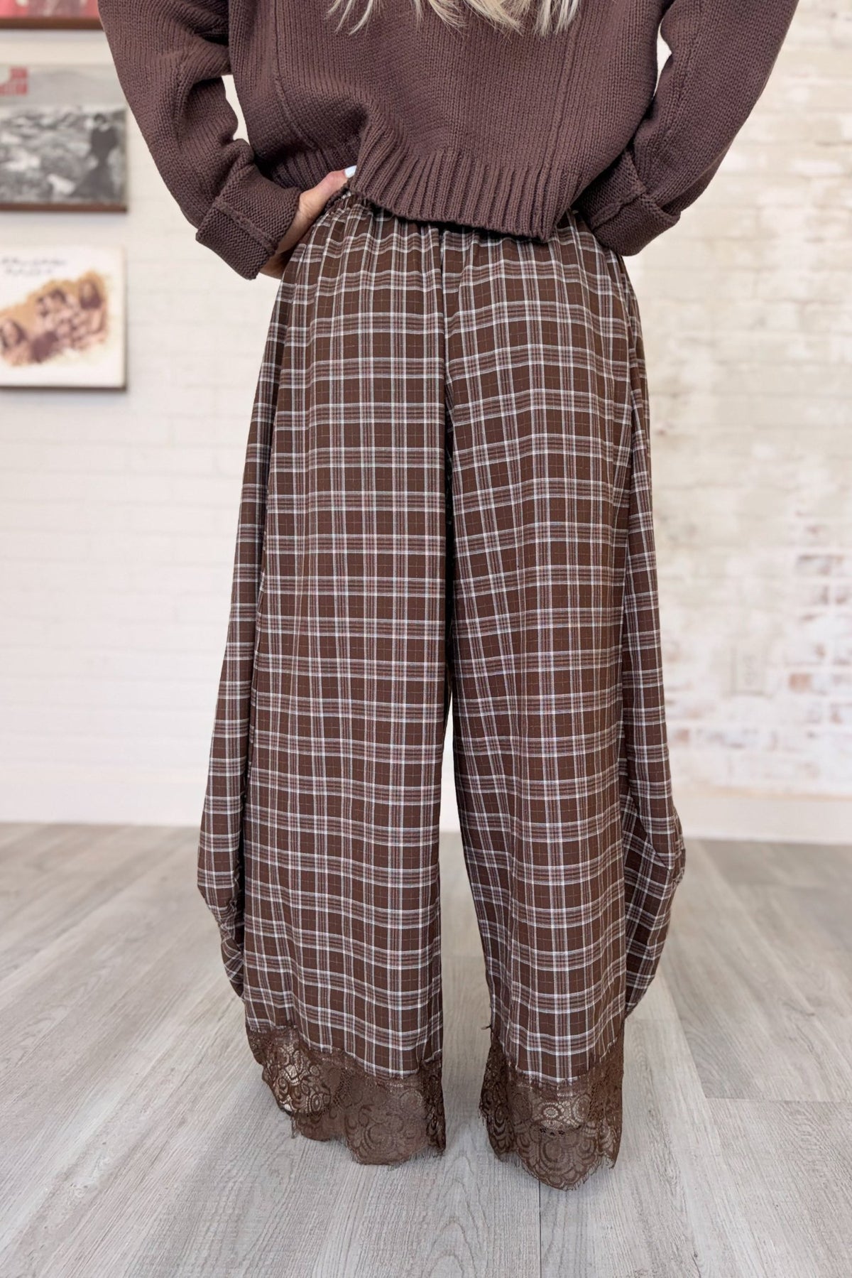 Women's brown and tan plaid wide-leg barrel pants featuring a relaxed, flowy silhouette, lightweight woven fabric, elastic waistband with adjustable drawstring, side pockets, and intricate chocolate brown floral lace trim along the hems. These boho-inspired, full-length plaid pants combine vintage romantic styling with a modern oversized fit, perfect for fall outfits, casual layering, and bohemian boutique fashion.