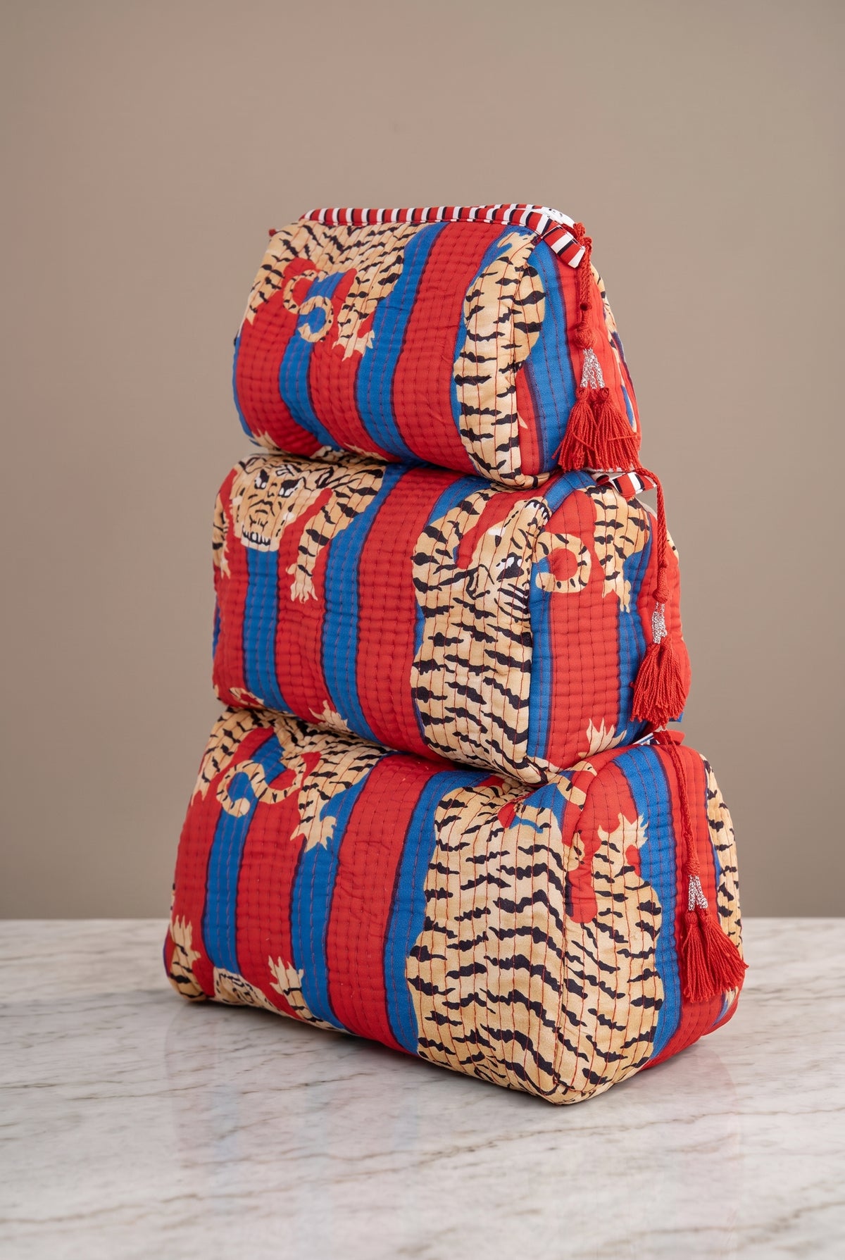 Red Roam If You Want To quilted tiger makeup bag set in three sizes with bold red and blue stripes, tiger print, and tassel zipper pulls.