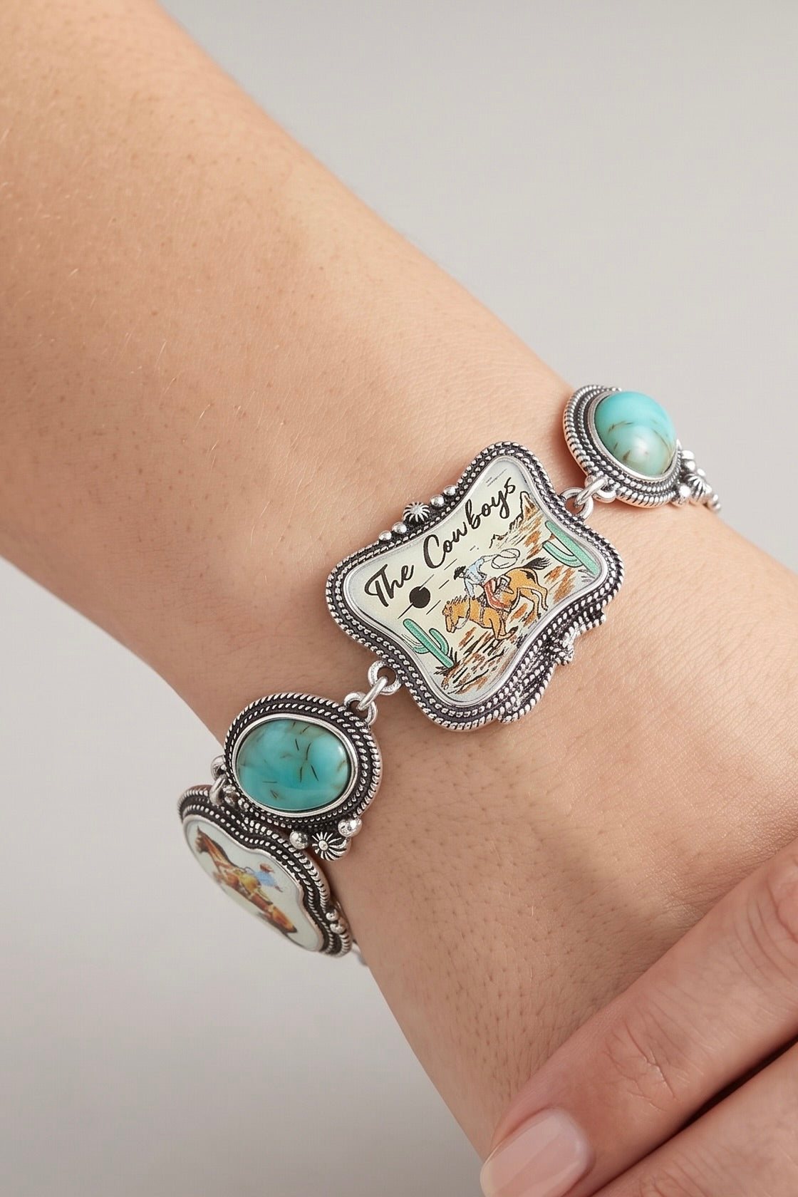 Western toggle bracelet featuring vintage cowboy scene panels, turquoise-look oval stones, antique silver detailing, and a statement toggle clasp.
